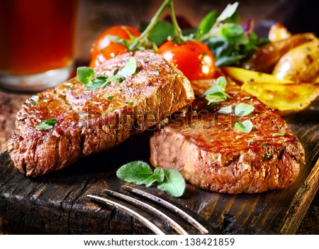 Succulent thick juicy portions of grilled fillet steak served with tomatoes and roast vegetables on an old wooden board Royalty-Free Stock Photo #138421859
