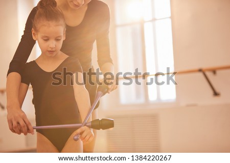 Portrait of unrecognizable woman teaching little girl doing gymnastics moves with clubs in studio lit by warm sunlight, copy space