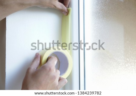 Man putting tape on the wall. The simple step for the quick and easy painting process. Renovation house concept.
