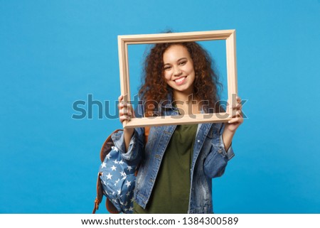 Young african american girl teen student in denim clothes, backpack hold frame isolated on blue background studio portrait. Education in high school university college concept. Mock up copy space