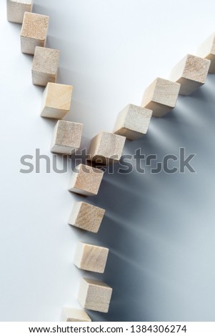 A long curved line of wooden cubes is divided into two, as a symbol of a queue, a competition for a position or a team, on an uneven white background.