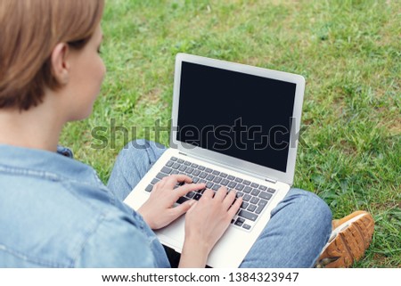 Young female student at university campus sitting on green grass browsing website back view laptop screen close-up