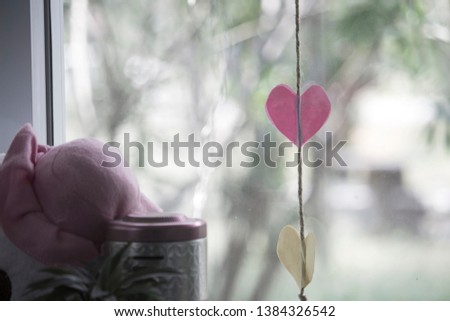 Paper heart with a string hanging on the window.Clear glass seen outside is blurred.In the concept of love, nostalgia and romance with a retro background