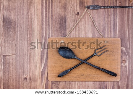 Wooden signboard hanging with spoon and fork on wall background