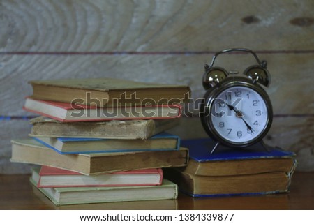 Old books stacked together with an antique alarm clock placed above Old wooden floor as background selective focus and shallow depth of field