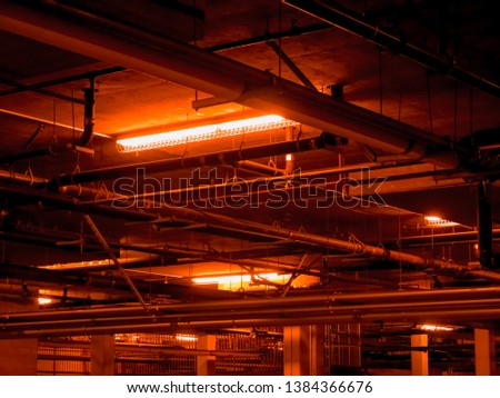 A lot of pipes inside the factory. Interior light at plant. Neon red lights in abandoned place. Many ceiling pipes running through tunnel. Heavy system of rusty tubes and pipes. Dark underground sewer