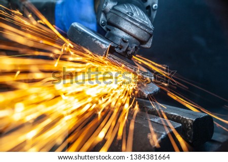 Close-up of a man sawing   bearing metal  hammer with a hand circular saw, bright flashes flying in different directions, in the background tools for an auto repair shop. Work of auto mechanics.