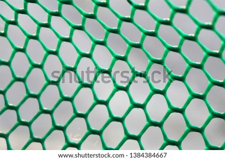 Close-up of green hexagonal colored mesh fence with a gray background.