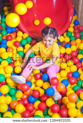 Happy little girl playing in colorful balls. Happy child playing at colorful plastic balls in play center