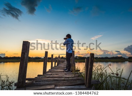 photographer on wooden bridge across the lake on sunset background