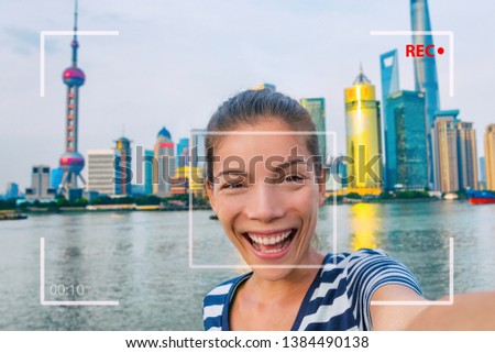 Happy China travel selfie Asian tourist woman vlogging online recording videoblog vlog video. Smiling young girl holding camera phone at the Bund at Shanghai's skyline of skycrapers.