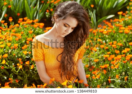 Healthy Long Curly Hair. Beautiful Brunette Woman over marigold flowers, outdoors portrait
