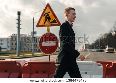young man in a suit is walking along a pedestrian crossing. on the road sign is under construction