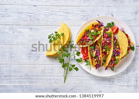 Mexican dish taco with meat, red cabbage, avocado, cherry tomatoes, corn, chilli, served on white plate, taco shell on a white wooden table, copy space, view from above, close up