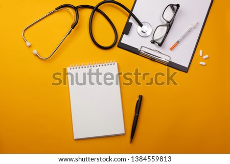 Stethoscope in doctors desk with notebook and pills. Top view with place for your text.