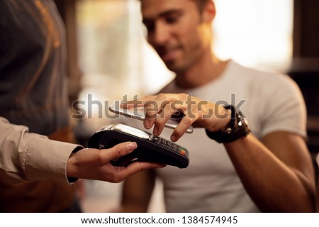 Close up of guest using smart phone while making contactless payment in a pub.  Royalty-Free Stock Photo #1384574945