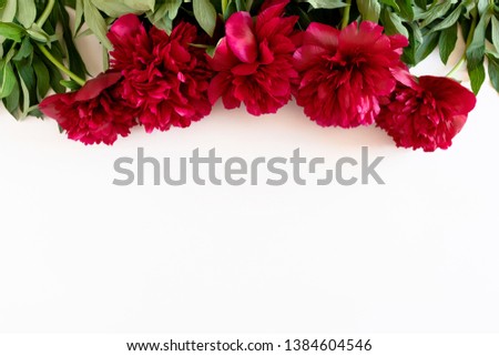 Border frame made of lush red peonies and green leaves on a white background