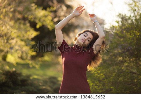 Beautiful young Armenian woman posing with closed eyes near green trees at sunset in a city park, camping without garbage