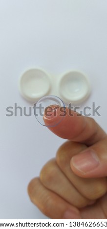 Clear contact lens on woman finger and another one in the bearing with cleaner solution.It is clean,ready to use for vision.They made for solve short or long sighted problems,do not have wear glasses.