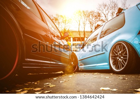 Two modified low cars in brown and light blue color. Stance custom cars with a forged polished wheels parked on a street at sunny day. Tuned automobiles Royalty-Free Stock Photo #1384642424