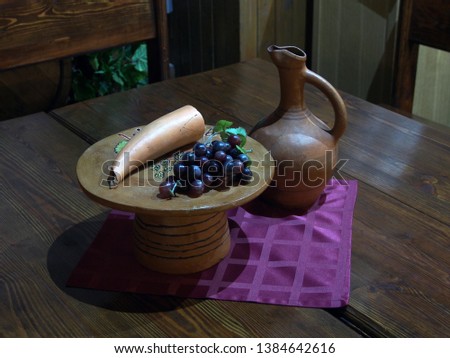 Pottery, a wine jug and a plate of grapes standing on a wooden table. Stylized village antiquity.