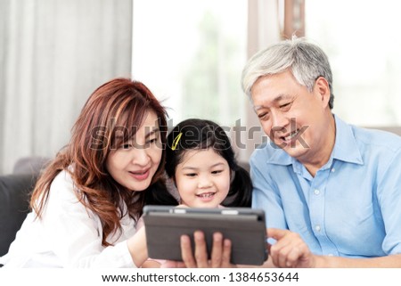 Grandparents and Granddaughter using technology digital tablet on sofa in living room. Happy asian Grandpa and Grandma using internet by tablet pc with little girls.