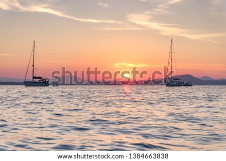 Sun setting down and hiding behind the mountains of Sardinia. The picture was taken from an anchoring yacht resting on the calm sea of La Maddalena