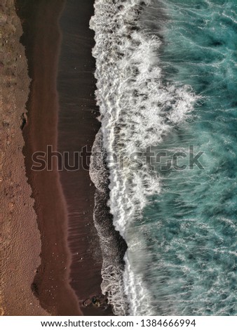 Birds eye view of the blue ocean water crashing in the black sand beach