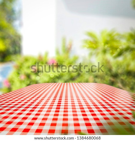 Tableclothe of red and white color and summer background of garden. Free space for your decoration. 