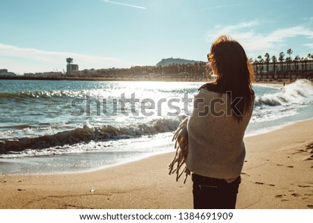 Young female adult standing in the sun next to the sea in strong daylight