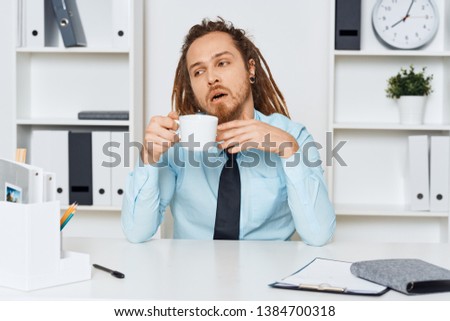 A business man in a shirt is sitting at a table in the office and drinking coffee                  