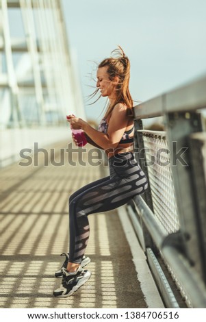 Young fitness woman is resting after hard training on the river bridge and drinking water.