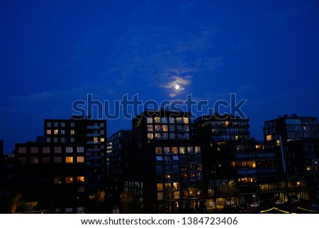 Full moon shining over modern buildings at night with lightened windows