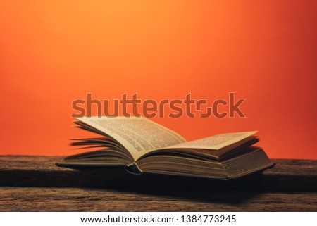 Old book on a old oak wooden table and coral orange wall background behind.