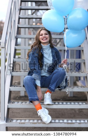 Young woman with balloons sitting on stairs outdoors