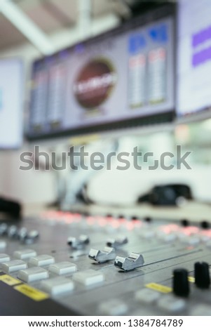 Close up picture of a soundboard in a broadcasting studio, computers in the blurry background