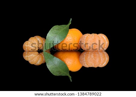 Peeled tangerines and tangerines in their skins with green leaves on black glass with bright and juicy reflection