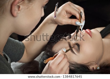 The master builds the lashes of the client in a beauty salon. Cosmetic procedures on eyebrows. A girl with a tweezers in his hands keeps the bill of lading.