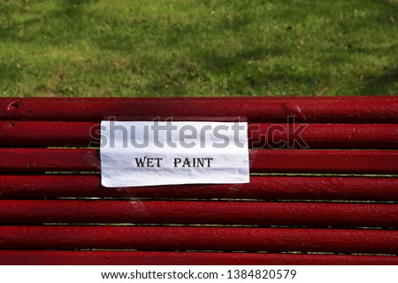English inscription 'Wet paint' on a sheet of white paper on red wooden bench, park improvement