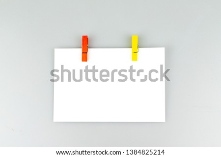 Blank white horizontal poster paper attached with red and yellow clips hung on white blackground.