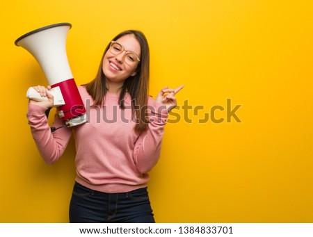 Young cute woman holding a megaphone pointing to the side with finger