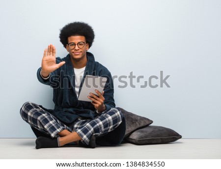 Young black man sitting on his house and holding his tablet putting hand in front