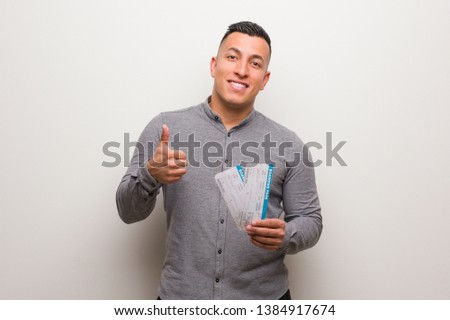 Young latin man holding an air tickets smiling and raising thumb up