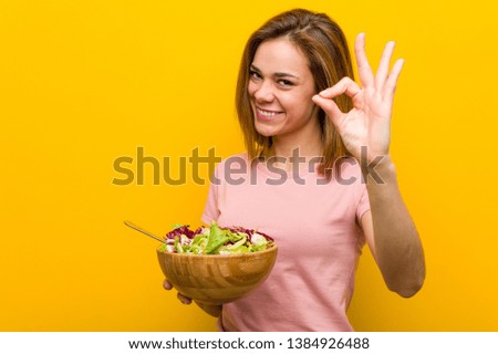 Young healthy woman holding a salad cheerful and confident showing ok gesture.