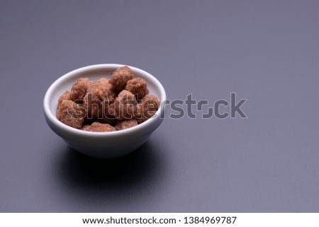 Peanuts praline sweet in a white bowl, on dark grey background, angle view, soft light, copy space