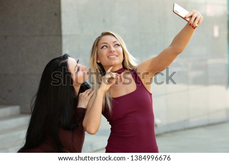 Cute outdoor portrait of funny pretty best friends girls having fun making selfie at city center.