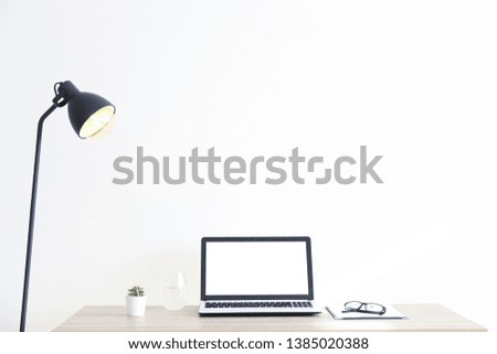 Blank screen laptop computer, cup of cappuccino coffee, cactus, supplies and folded eye glasses on wooden desk in spacious office full of sunlight. Creative workspace. Close up, copy space, background
