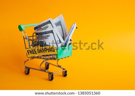 Shopping cart on orange background with money and airplane in it, one hundred dollars in shopping cart