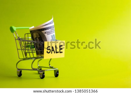 Sale concept, shopping cart with words "Sale" on green background, dollars in shopping cart