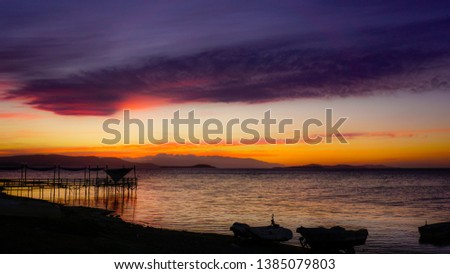 Dramatic sunset landscape at Urla, Izmir, Turkey. Beautiful blazing sunset landscape over bright blue sea and orange cloudy sky above it with awesome golden rays of sun light reflection on calm waves.